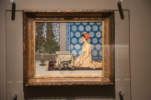 Osman Hamdi Bey'in Genç Kadın Okurken adlı eseri bir camın arkasında duvarda asılı bir şekilde